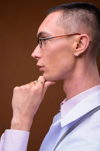 Young handsome androgynous man doctor against brown background