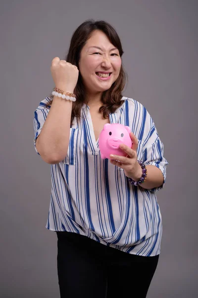 Zralé krásné asijské podnikatelka drží prasátko — Stock fotografie