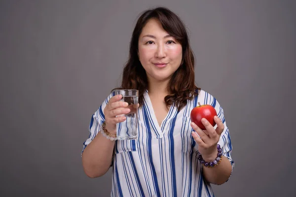 Empresaria asiática sosteniendo vaso de agua y manzana — Foto de Stock