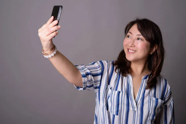 Zralé krásné asijské podnikatelka s selfie s telefonem — Stock fotografie