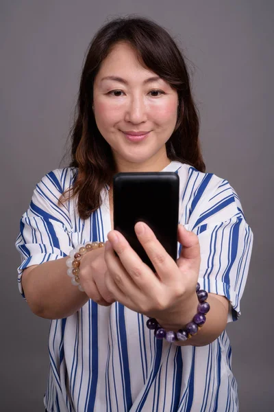 Zralé krásné asijské podnikatelka pomocí mobilního telefonu — Stock fotografie
