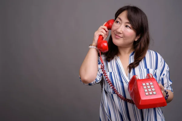 오래 된 빨간 전화를 들고 성숙한 아름 다운 아시아 사업가 — 스톡 사진