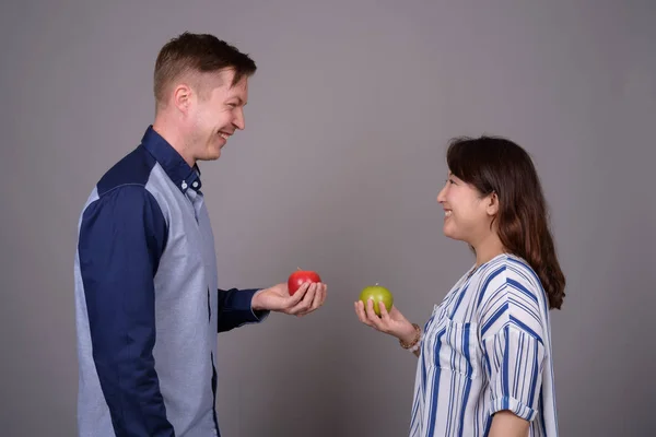 Couple multi ethnique diversifié en studio tenant des pommes vertes et rouges — Photo