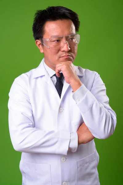 Dojrzały człowiek japoński lekarz okularów ochronnych na zielonym tle — Zdjęcie stockowe