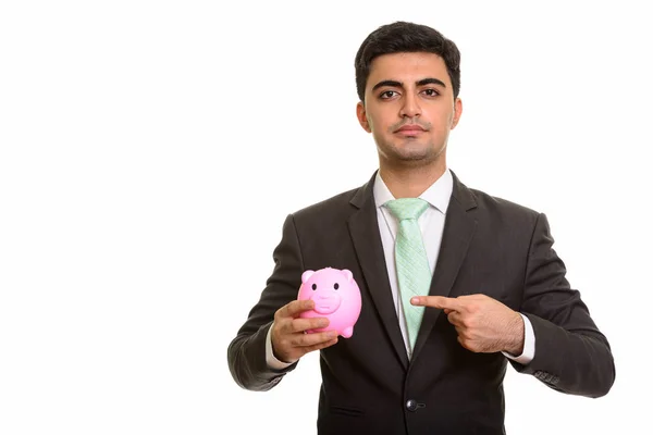 Young handsome Persian businessman holding piggy bank and pointi — Stock Photo, Image