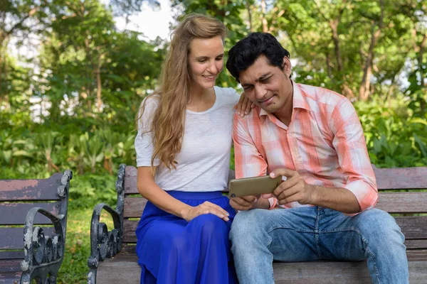 Feliz pareja multi étnica sonriendo mientras se utiliza el teléfono móvil y s — Foto de Stock