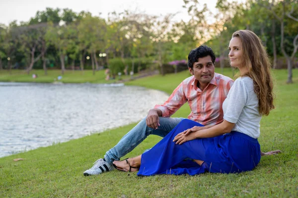 緑の公園の湖の景色に対して牧草地に座っている間 複数の民族のカップルの思考 — ストック写真