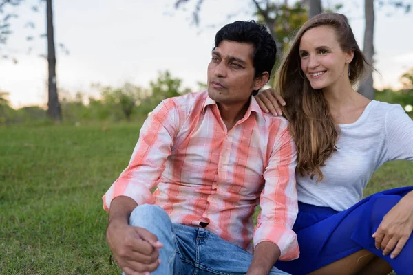 Feliz pareja multi étnica sonriendo mientras piensa y se sienta en — Foto de Stock