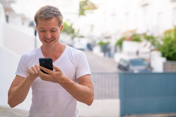 Ευτυχισμένος όμορφος νεαρός χρησιμοποιώντας τηλέφωνο σε εξωτερικούς χώρους στους δρόμους — Φωτογραφία Αρχείου