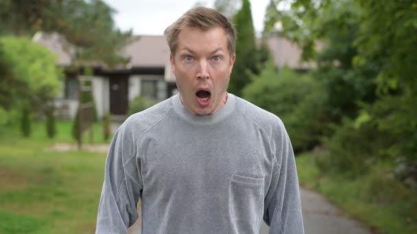 Jovem bonito homem olhando surpreso e cobrindo boca em casa ao ar livre — Vídeo de Stock