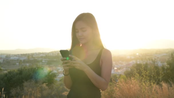 Młody szczęśliwy turystyczne Azji kobieta myślenia przy użyciu telefonu na wzgórzu — Wideo stockowe