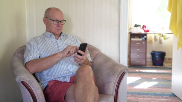 Hombre mayor feliz usando el teléfono en el sofá en casa — Vídeo de stock