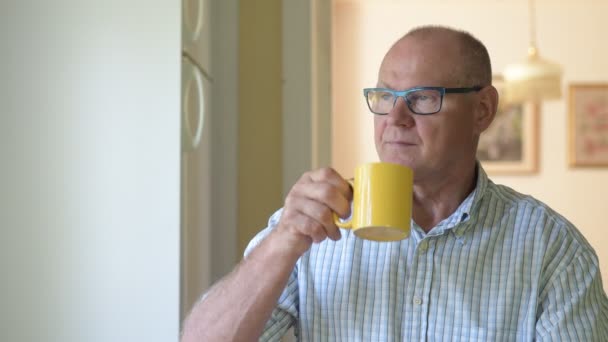 Продуманий старший чоловік п'є каву під час перегляду вікна — стокове відео