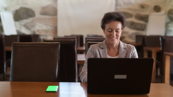 Glücklich reife Geschäftsfrau mit Telefon und Laptop in der Kaffeestube — Stockvideo