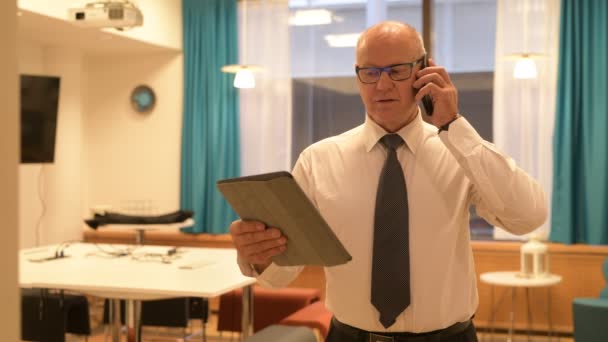 Empresario senior que usa tableta digital mientras habla por teléfono en el trabajo — Vídeos de Stock