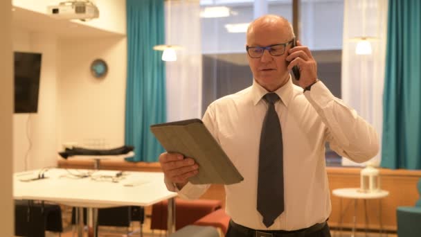 Senior affärsman använder digitala surfplatta medan du talar i telefonen på jobbet — Stockvideo