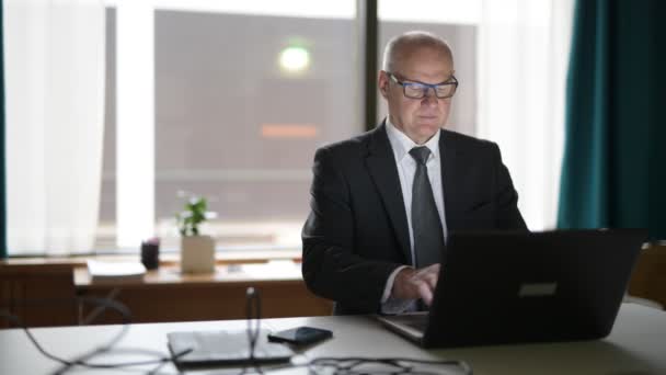 Zufriedener Senior-Geschäftsmann mit Telefon und Laptop bei der Arbeit — Stockvideo