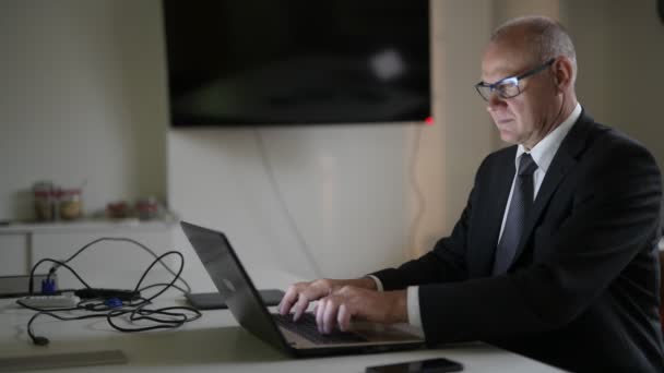 Ευτυχής ανώτερος επιχειρηματίας χαμογελώντας ενώ χρησιμοποιώντας τηλέφωνο και φορητό υπολογιστή στο χώρο εργασίας — Αρχείο Βίντεο