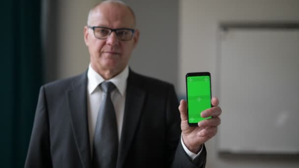 Glücklicher Senior-Geschäftsmann zeigt Telefon am Fenster im Büro — Stockvideo