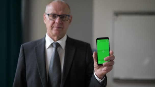 Glad Senior affärsman visar telefonen genom fönstret på kontoret — Stockvideo