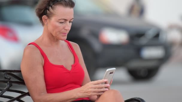 Zralá žena šťastná turistické pomocí telefonu, zatímco sedí na lavičce — Stock video