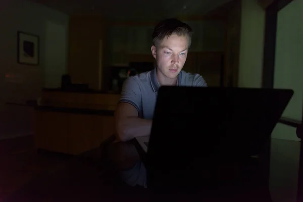 Fiatal jóképű férfi használ laptop a sötét nappaliban — Stock Fotó
