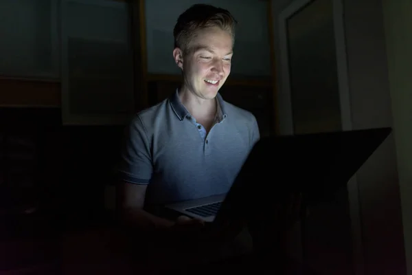 Fiatal jóképű férfi használ laptop a sötét nappaliban — Stock Fotó