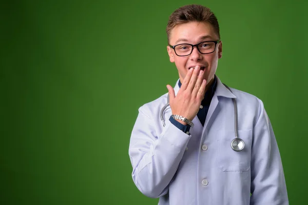 Junger schöner Mann Arzt vor grünem Hintergrund — Stockfoto