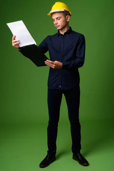 Joven hombre de negocios guapo con hardhat sobre fondo verde —  Fotos de Stock