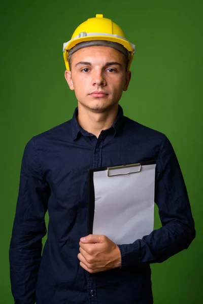 Ung snygg affärsman med hardhat mot grön bakgrund — Stockfoto