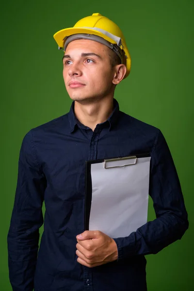 Ung snygg affärsman med hardhat mot grön bakgrund — Stockfoto