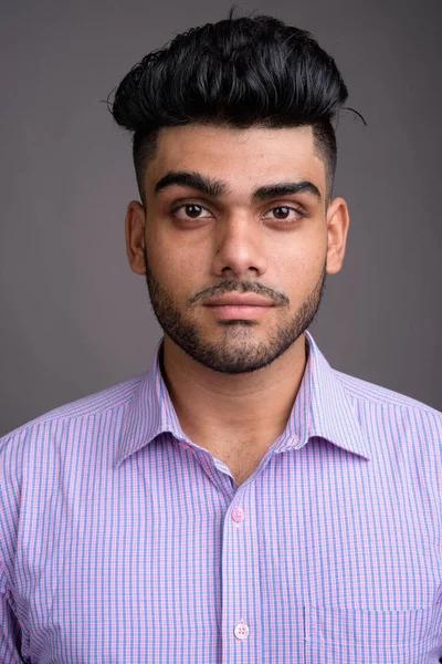 Young handsome Indian businessman against gray background