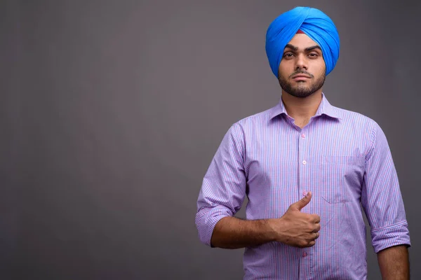 Mladý pohledný indický podnikatel nosí turban proti šedé ba — Stock fotografie
