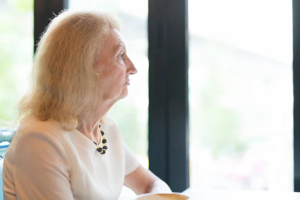 Senior äldre kvinna tittar genom fönstret — Stockfoto