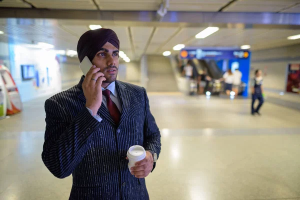 Young handsome Indian Sikh businessman at subway train station talking on phone