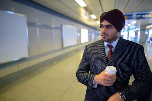 Young handsome Indian Sikh businessman at subway train station holding coffee cup — Stock Photo, Image