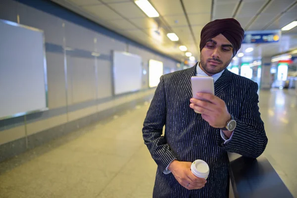 นักธุรกิจชาวอินเดียที่สถานีรถไฟใต้ดินใช้โทรศัพท์มือถือและถือถ้วยกาแฟ — ภาพถ่ายสต็อก