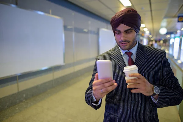 Indian businessman at subway train station using mobile phone and holding coffee cup — Stock Photo, Image