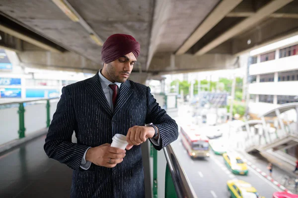 Indian Sikh businessman checking smart watch and holding coffee — Stock Photo, Image