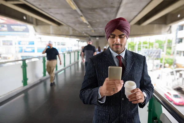 Indian businessman using mobile phone and holding coffee cup in city