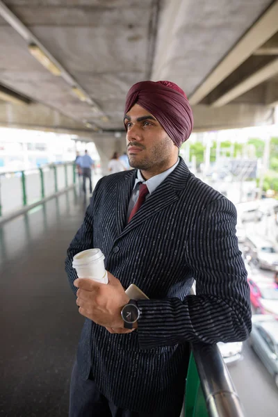 Young handsome Indian Sikh businessman holding coffee cup