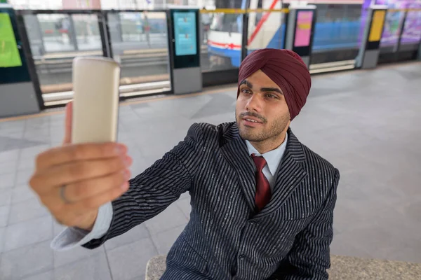 Indian businessman sitting at train station while taking selfie with mobile phone — Stock Photo, Image