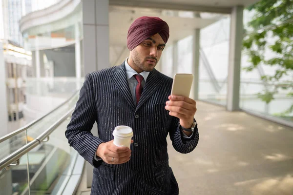 Indian businessman in city holding coffee cup and mobile phone