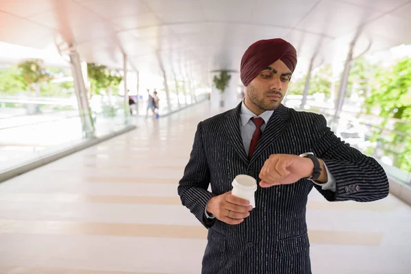 Indian Sikh businessman checking smart watch and holding coffee — Stock Photo, Image