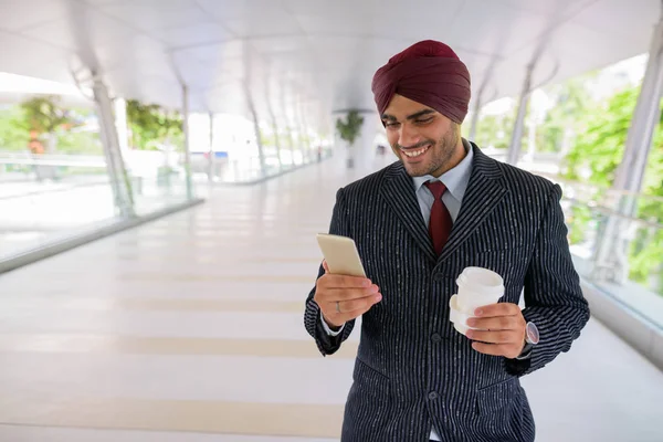 Indian businessman in city using phone and holding coffee cup — Stock Photo, Image
