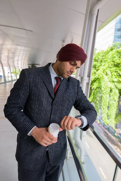 Indian Sikh businessman checking smart watch and holding coffee — Stock Photo, Image