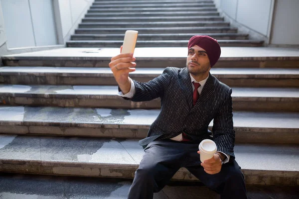 Homme d'affaires indien assis sur les escaliers tout en utilisant le téléphone et en buvant du café — Photo