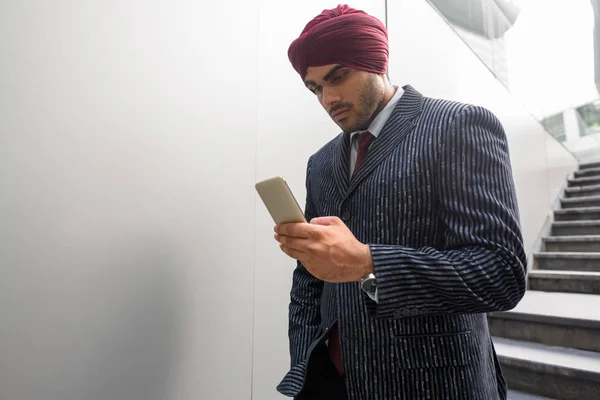 Portrait of Indian businessman with turban outdoors in city using phone — Stock Photo, Image
