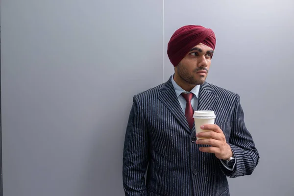 Indian businessman outdoors in city holding coffee cup while thinking