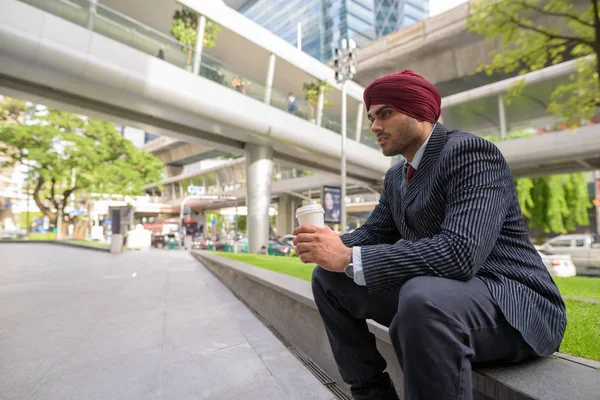 Indian businessman sitting outdoors in city while having coffee break